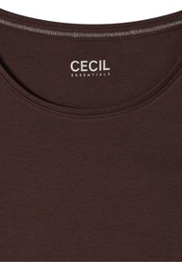 Tissu brun foncé avec encolure courbée montrant le nom de la marque imprimé en blanc "CECIL ESSENTIALS" à l'intérieur du col.