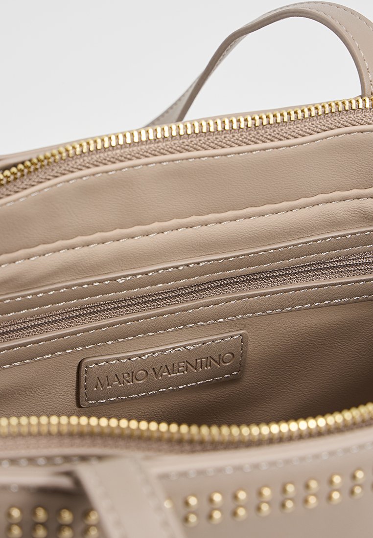 Bolso de mano de cuero beige con interior texturizado, compartimentos con cremallera, herrajes en tono dorado y acentos con tachuelas. La etiqueta dice "Mario Valentino."