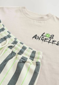 Lichtroze T-shirt met een zwart "LOS ANGELES" graphic. Grijs-witte gestreepte shorts met groene accenten en een elastische tailleband.