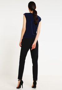 Námořnický modrý top s krátkým rukávem spárovaný s černými slim-fit kalhotami a vysokými podpatky. Hladká látka s minimálními švy.