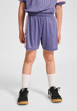 Lilla træningsshorts med lodrette striber, elastisk taljebånd og lyserøde detaljer i siden, kombineret med sorte sneakers og hvide sokker.