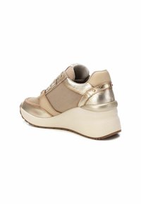 Zapatillas cuña en color beige claro con acentos dorados metálicos, paneles de malla texturizada y tachuelas decorativas. Suela acolchada para mayor apoyo.