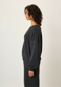 Sweatshirt noir surdimensionné avec des manches texturées, col rond et épaules drop. Fabriqué en tissu doux, avec des coutures minimales et une coupe décontractée.