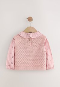 Lyserød strikket top med et tekstureret diamantmønster, puffede ærmer med blomstret broderi og en flæsekantet krave med knaplukning bagpå.