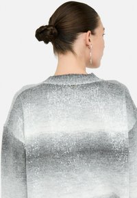 Pulover ombre gri cu paiete metalice, are un decolteu rotund și un detaliu de marcă vizibil pe spate. Textură moale și croială relaxată.