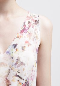 Ärmlös klänning med V-ringning, tillverkad av lätt tyg med ett pastellfärgat fjärilstryck i olika färger, inklusive rosa och blått.