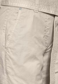 Pantalons en coton beige avec une ceinture texturée à la taille, dotés de poches latérales et de détails de couture subtils. Tissu lisse avec une coupe décontractée.