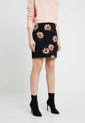 Falda negra con patrón floral en tonos rosas; diseño ajustado. Combinada con un suéter rosa claro y botas de tobillo negras. Textura de tela suave.