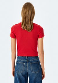 Rød ribbet kortærmet crop top parret med højtaljede blå denim jeans. Stoffet er blødt med en struktureret finish.