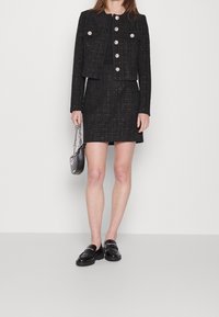 Veste en tweed noir avec boutons argentés et jupe assortie. Présente un design ajusté, une texture lisse et comprend un petit sac à main gris.