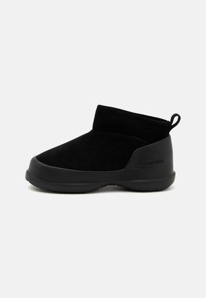 Stivaletti neri alla caviglia con tomaia in suede liscio e suola in gomma, caratterizzati da un design minimalista e un'impugnatura sul retro per facilitarne l'indossamento.