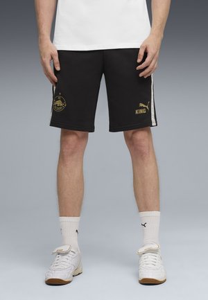 Svarta sportshorts med guldtryck och texten "KING", vita sidostråkar, matchade med vita sneakers och ankellånga strumpor.