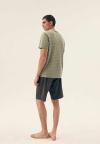 Jasnozielona koszulka w paski z okrągłym dekoltem, zestawiona z ciemnymi szortami. Minimalistyczny design, miękka tkanina i prosty krój. Model stoi na boso.