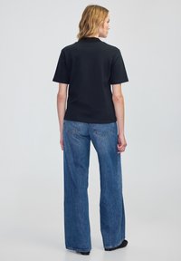 Černé polo tričko s krátkým rukávem spárované s volnými modrými denimovými džíny s rovný střih a jemným vyblednutím látky.