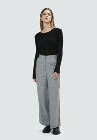 Maglietta nera a coste con maniche lunghe abbinata a pantaloni larghi a quadri grigi a vita alta con strisce gialle sui lati e scarpe platform nere.
