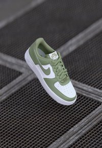 Nike Air Force 1 sneakers med grøn læderoverflade og hvide detaljer, rund tå, perforeringer og tekstureret ydersål.
