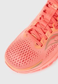 Chaussure de course légère en corail vif avec une tige en mesh, des détails texturés et une semelle rembourrée. Comprend des lacets plats et des accents de logo.