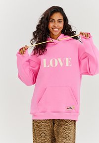 Růžová oversized mikina s potiskem "LOVE" v krémovém písmu, s přední kapsou a zlatými doplňky na tkaničce. V soutěži s leopardími kalhotami.