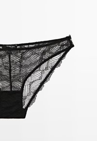 Sort blonde trusse med blomsterprint, gennemsigtig tekstur og bølgede kanter. Mærket synligt: Massimo Dutti, størrelse L.