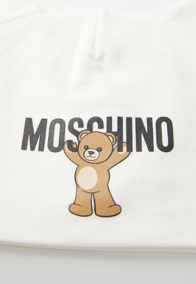 White fabric featuring a printed brown bear with a light tan belly and black text reading "MOSCHINO" above the bear. Text and bear are central.