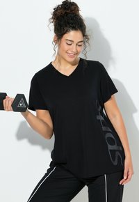 Camiseta negra de manga corta con cuello en V y estampado texturizado de "sport" en el lateral. Se lleva con pantalones negros que tienen franjas blancas en los costados.