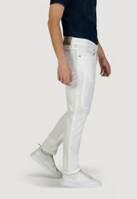 Pantaloni in denim bianco con vestibilità slim, tasche frontali, hardware argentato e un motivo sottile. Abbinati a sneakers bianche e una maglietta blu scuro.