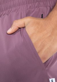 Ljuslila shorts med elastisk midja, med en sidoficka där en hand är inskjuten. Slät textur, minimala design detaljer.