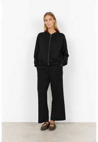 Black zip-up sweatshirt with a round neckline, paired with wide-leg black pants. Both garments feature a smooth, soft texture.
