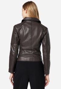 Braune Leder-Motorradjacke mit gesteppten Schulterakzenten, tailliertem Design und einem eingeschnittenen Kragen, der eine glatte, glänzende Textur zur Schau stellt.