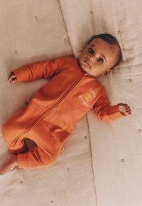 Body en coton côtelé orange pour bébé avec fermeture éclair sur le devant et manches longues, arborant un motif brodé "petit potiron". Tissu doux et texturé.