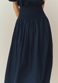 Tmavomodrá sukňa s nariaseným pásom, ktorá má vzdušný strih a skladanú štruktúru, vyrobená z ľahkej látky.