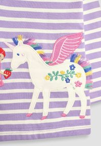 Lilla og hvidstribet stof har en hvid enhjørning broderi med lyserøde vinger, levende manke og blomsterdetaljer.