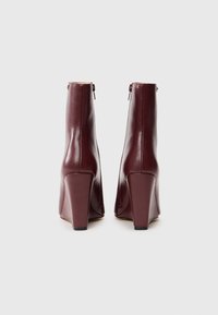 Bottes en cuir bordeaux à cheville avec un bout carré, un haut talon bloc et une fermeture éclair à l'arrière. Fini texturé avec des accents lisses.