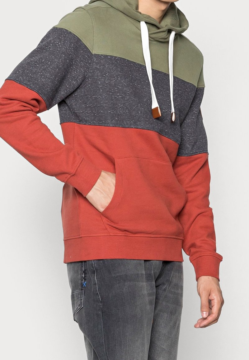 Sudadera con capucha con bloques de color verde, azul oscuro y rojo. Presenta un bolsillo frontal, cordones blancos y una textura de tela.