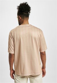 Cămașă scurtă cu mânecă, de culoare roz deschis, cu dungi verticale subțiri albe. Textură netedă, croială lejeră și un design clasic cu gât rotund.