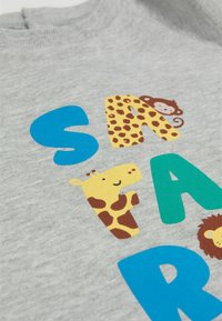 Szara bluza z kolorowymi grafikami zwierząt: małpą, żyrafą i lwem, z niebieskimi i zielonymi literami układającymi się w słowo "SAFARI."