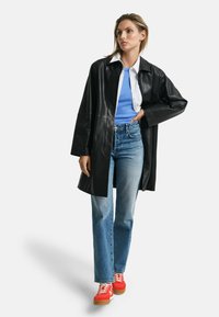 Schwarze Lederjacke, weißes Hemd mit Kragen, blaues T-Shirt, hochgeschnittene hellblaue Jeans und rote Sneakers mit weißen Akzenten.