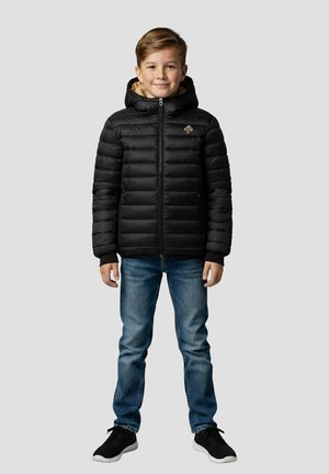 Zwarte pufferjas met capuchon, ritssluiting en doorgestikt ontwerp. Heeft een zandkleurige, met bont gevoerde kraag. Gecombineerd met een blauwe spijkerbroek en zwarte sneakers.