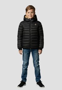 Sort dunjakke med hætte, lynlås og quiltet design. Har en lysebrun, pelsforet krave. Kombineret med blå jeans og sorte sneakers.