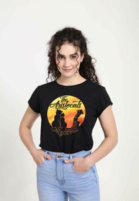 Sort t-shirt med "De Aristokatte" grafisk design i gul og orange, med karakterer kontureret mod en cirkulær solnedgang.