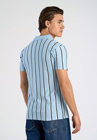 Ljust blå polo med vertikala svarta ränder, korta ärmar och krage. Materialet verkar vara slätt med en figursydd design.