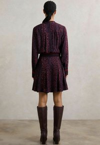 Sukienka w purpurowy i czerwony wzór węża z długimi rękawami, z paskiem w talii i rozkloszowanym dołem. Zestawiona z wysokimi, ciemnobrązowymi, obcasami do kolan.