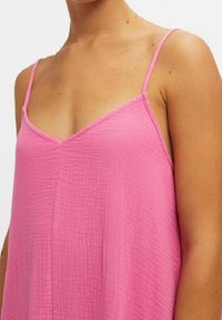 Haut sans manches rose en tissu texturé, avec un décolleté en V et des bretelles fines, tombant de manière fluide sur le corps.