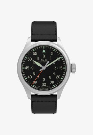 Timex óra fekete számlappal, ezüst tok, zöld fluoreszkáló mutatók, narancssárga másodpercmutató, fekete bőr szíj és ötperces lépésekben jelzett percekkel.