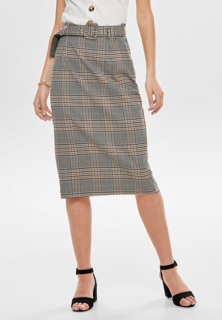 Femme portant une jupe crayon à carreaux longueur genou avec une ceinture assortie, un chemisier blanc sans manches avec des boutons et des talons noirs à bride cheville.