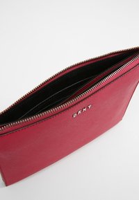 Red leather zippered clutch bag featuring a smooth texture, black interior lining, and a silver logo on the front.