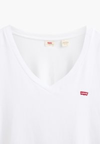 Balta kokvilnas T-krekls ar V veida kakla izgriezumu un nelielu sarkanu Levi's logotipu uz krūtīm. Apkakles iekšpusē redzamas birkas.