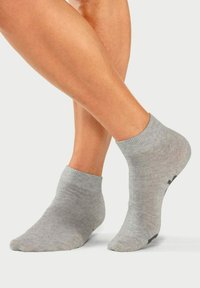 Calcetines de tobillo grises con una textura suave, que presentan una parte superior acanalada y un acento negro en la suela. Colocados sobre pies desnudos, destacando el ajuste.