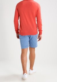 Sweter z koralików, niebieskie szorty z małymi białymi wzorami żaglówki i białe trampki. Przytulne materiały, luźny krój, żywe kolory.