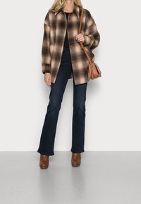 Ruskea ruudullinen ylisuuri paitajakku, tummat farkut, ruskeat korkokengät ja pieni nahkainen olkalaukku. Sileä pinta; nappisuljenta.